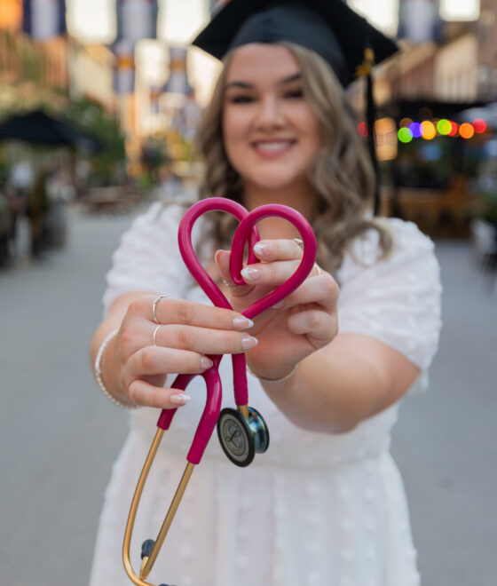 Female with a graduation cap holding a stethoscope in the shape of a heart.