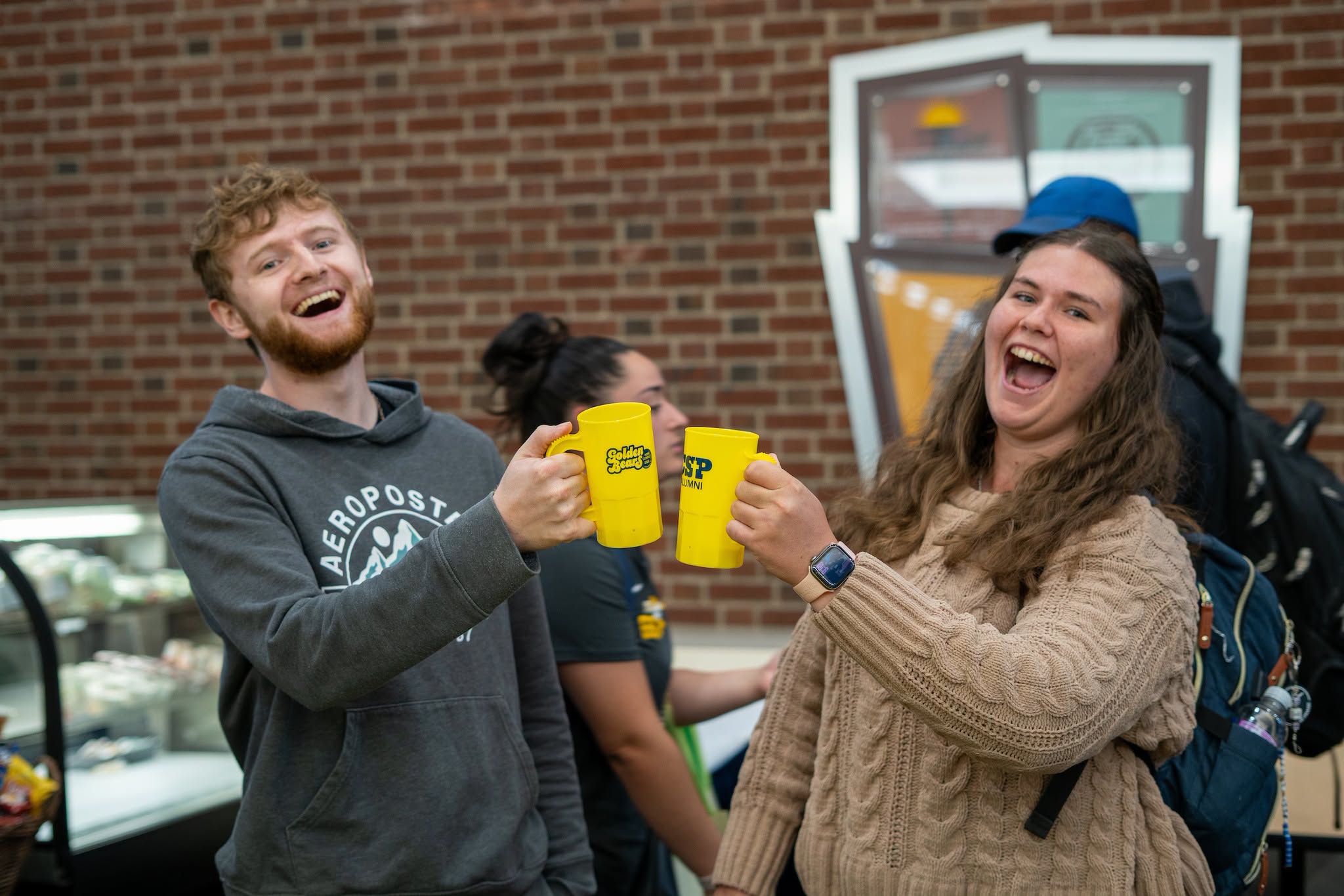 Two students doing "cheers" with homecoming mugs