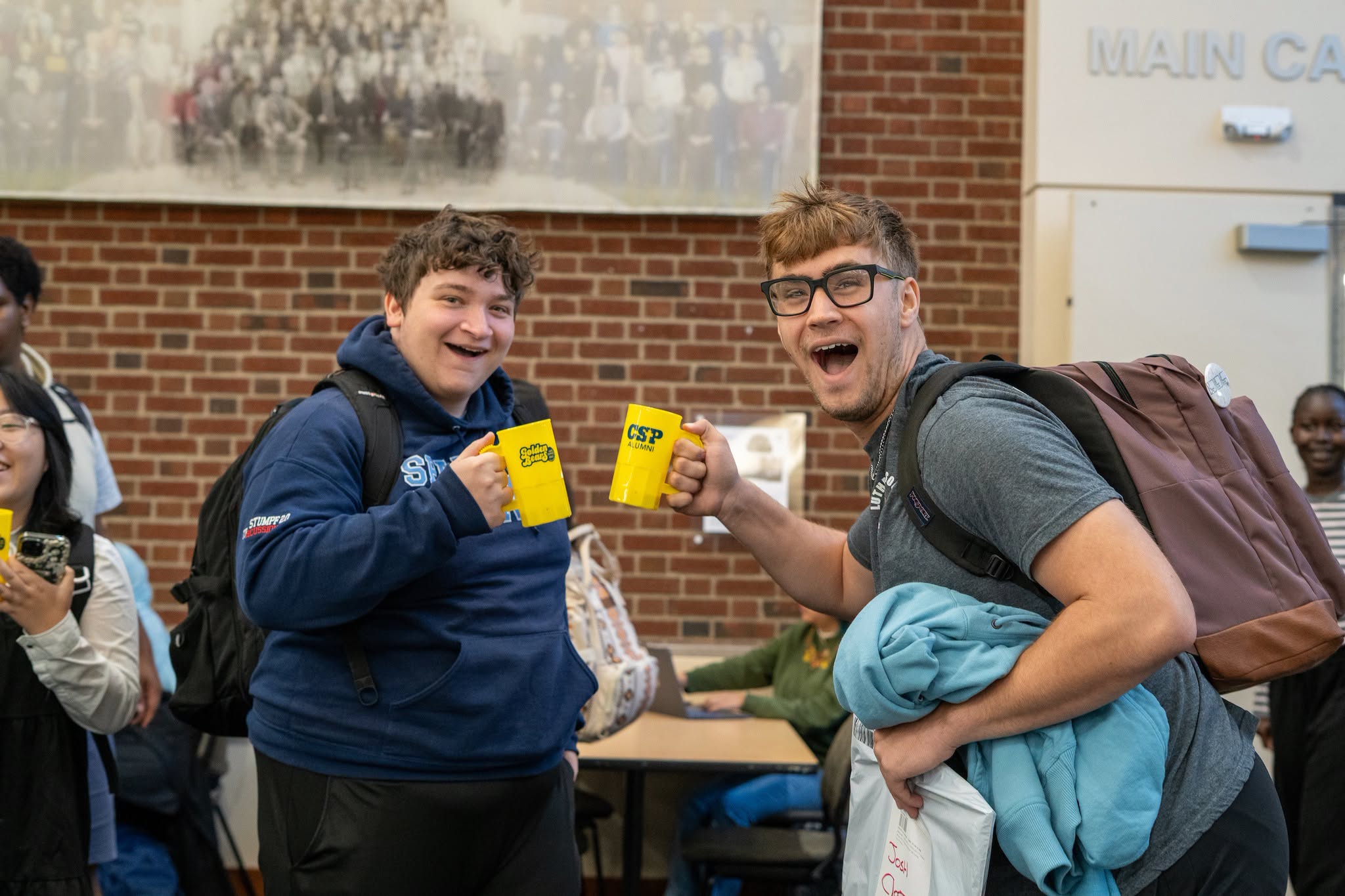Two students doing "cheers" with homecoming mugs